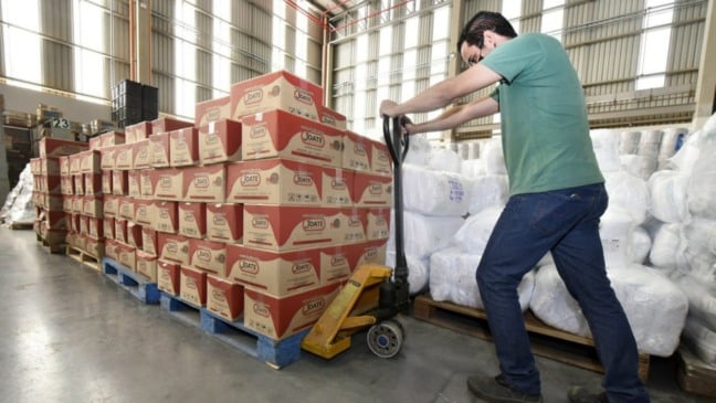 Homem puxando paleteira com doações de cestas básicas.