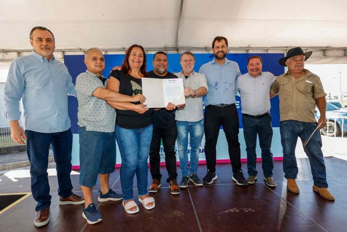 Entrega de escrituras no Jardim Novo Horizonte: Grupo de pessoas comemorando a regularização fundiária com documento oficial em mãos.
