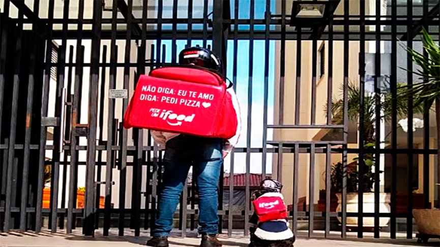 Entregador de aplicativo junto com cachorrinho na frente do prédio