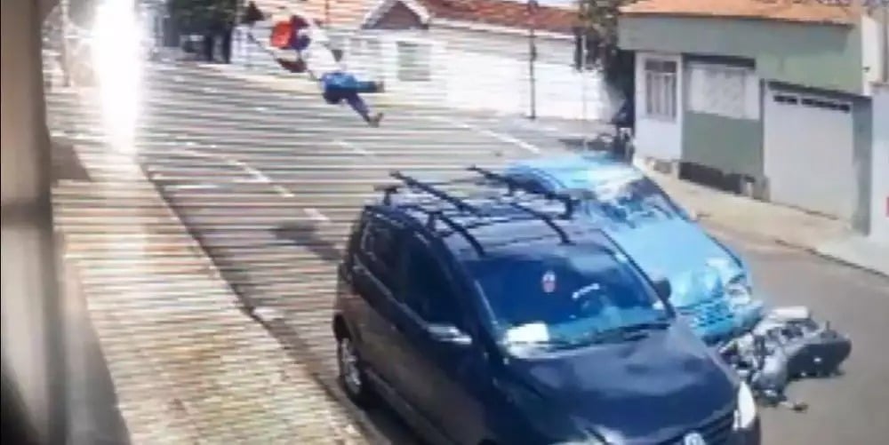 Frame de vídeo de segurança de entregador sendo arremessado após colisão com carro.