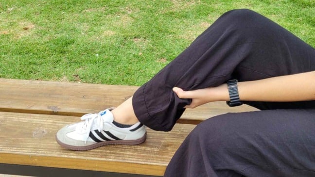 Perna de pessoa sob banco de praça.