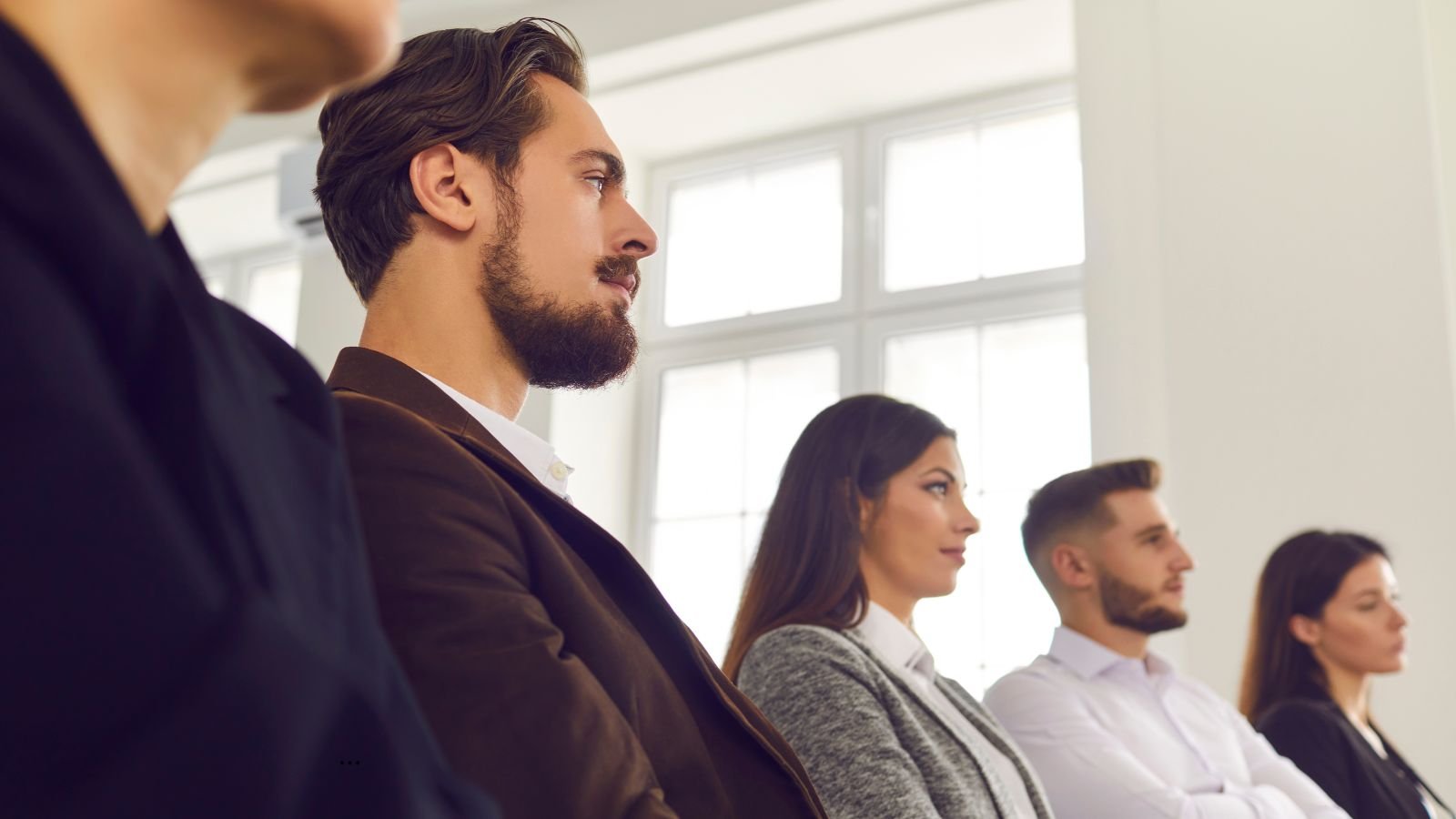 Grupo de jovens profissionais sentados em ambiente corporativo, atentos a uma apresentação.