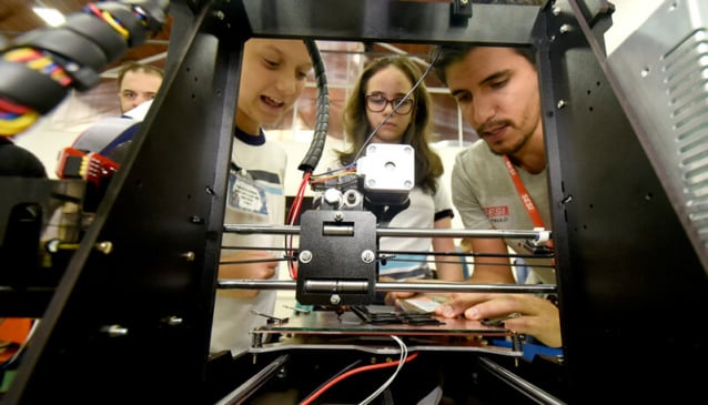 Alunos mexem em máquina com professor no FabLab