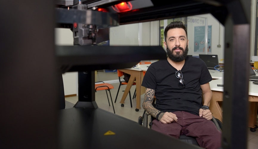 Foto de cadeirante em frente de impressora 3D