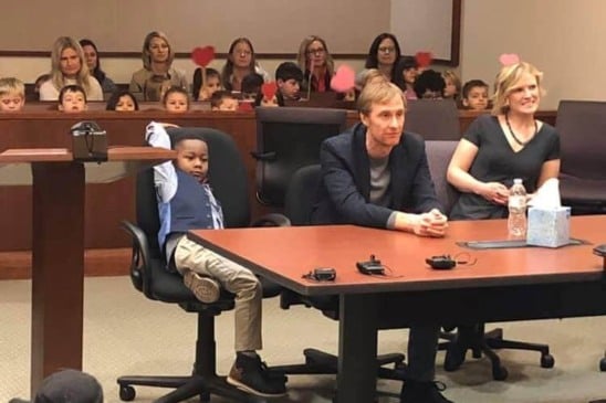 Michael e seus pais adotivos estão sentados à mesa; atrás, toda a sala de Michael segura corações desenhados