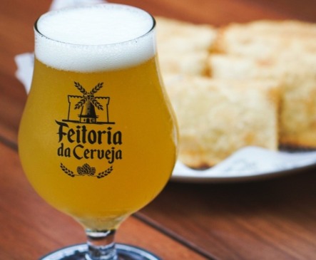 Taça de cerveja clara com porção pasteis ao fundo
