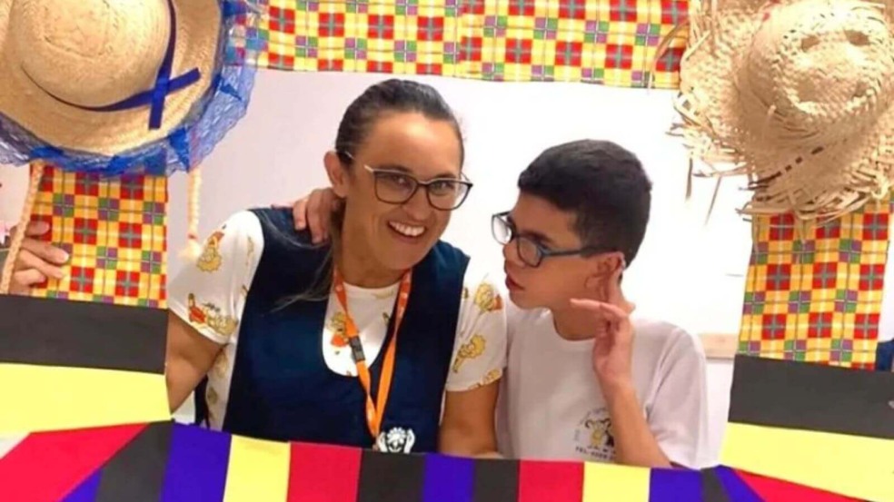 Professora e aluno posam em festa junina escolar, decorados com bandeirinhas e chapéus de palha na APAE Jundiaí