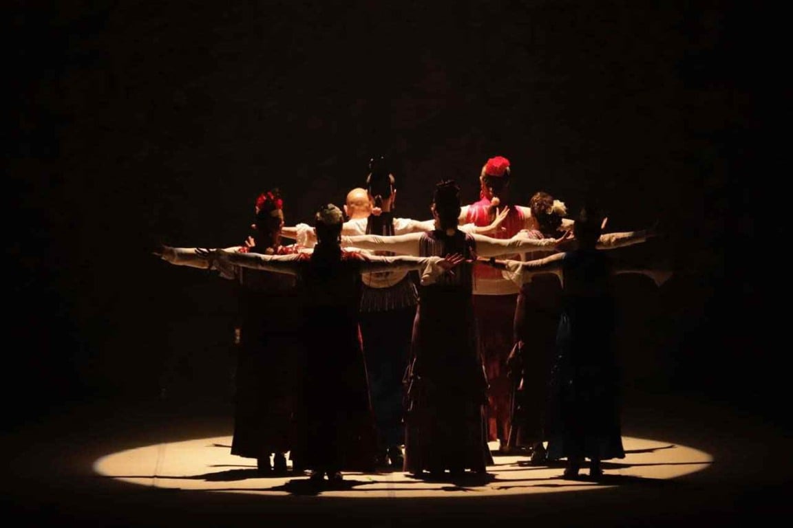 Espetáculo Sons y Sonidos: dançarinos flamencos em círculo com braços estendidos, iluminados por luz suave no palco da Sala Glória Rocha.