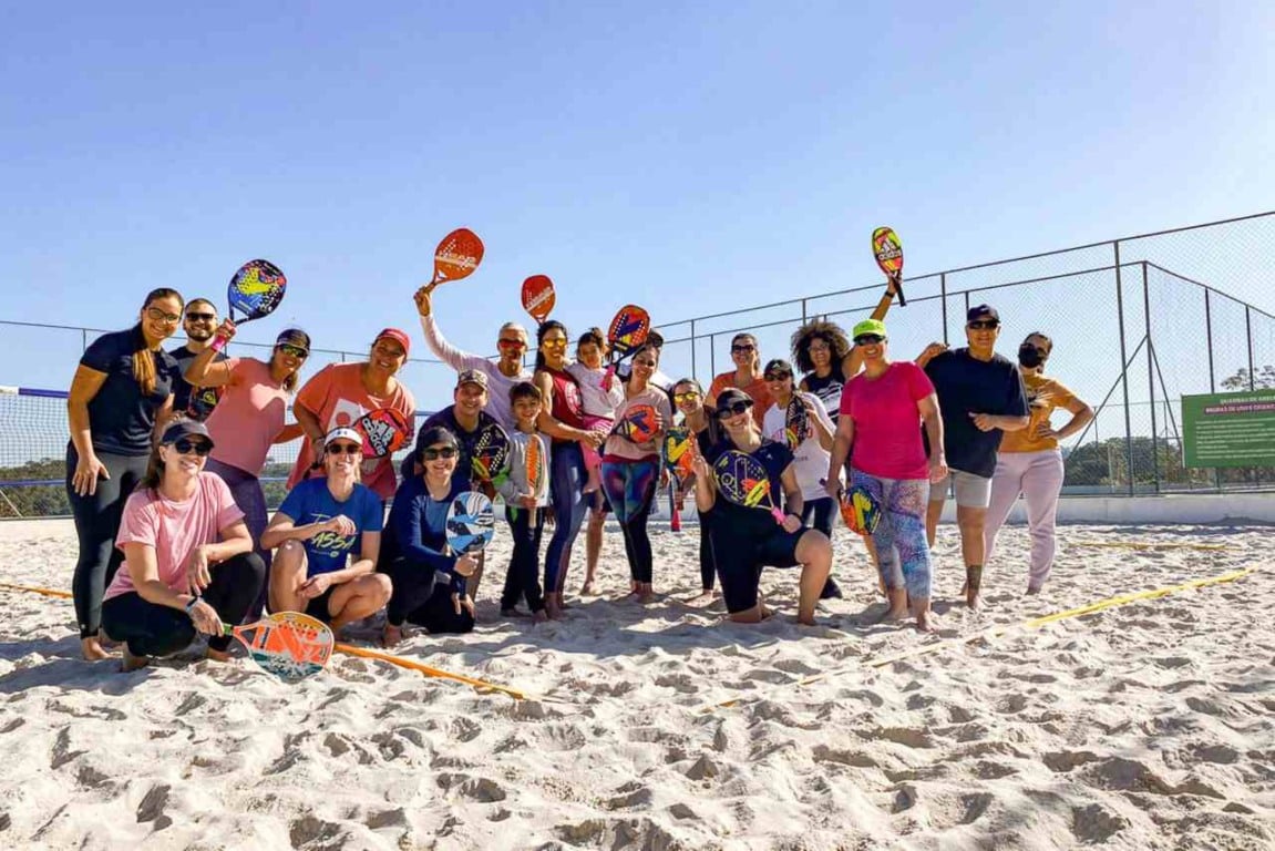 Grupo de adultos segurando raquetes em quadra de areia durante aula gratuita de Beach Tennis em Jundiaí.