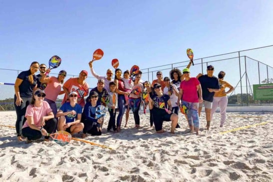 Grupo de adultos segurando raquetes em quadra de areia durante aula gratuita de Beach Tennis em Jundiaí.
