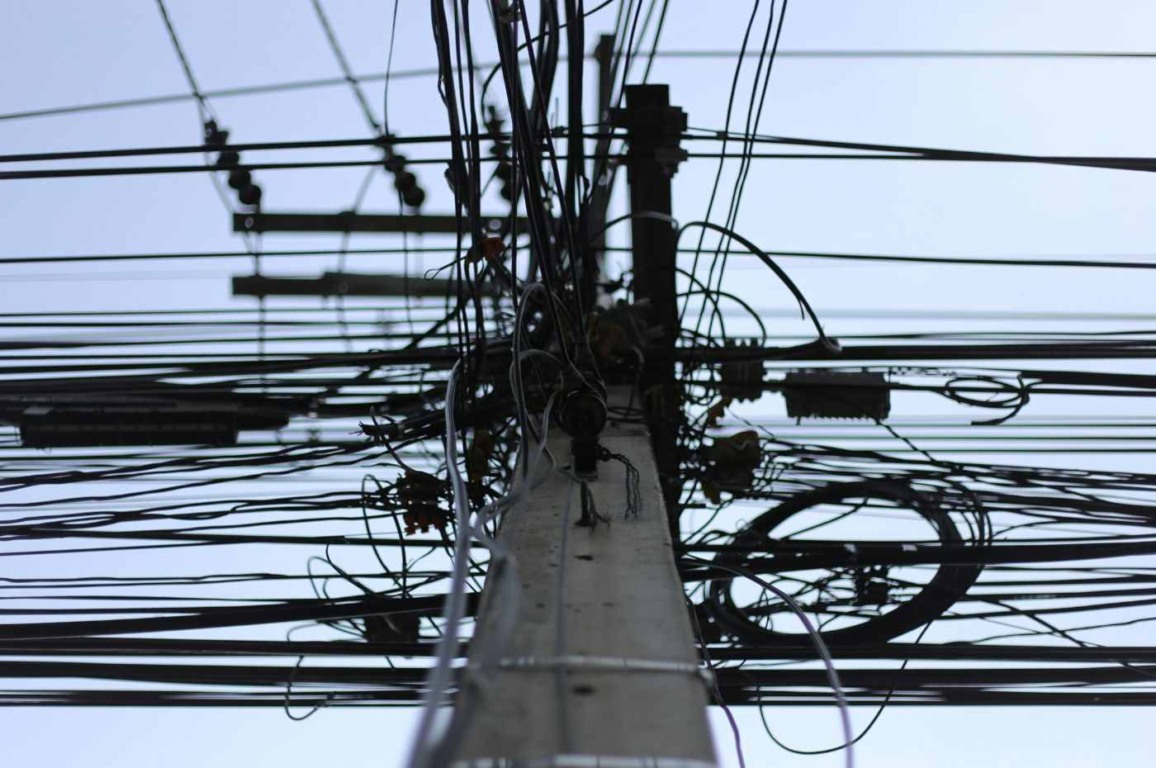Poste de energia elétrica com fiação embaraçada, representando furtos de energia ("gatos"), que impactam a conta de luz. Poste de energia elétrica com fiação embaraçada, representando furtos de energia ("gatos"), que impactam a conta de luz.