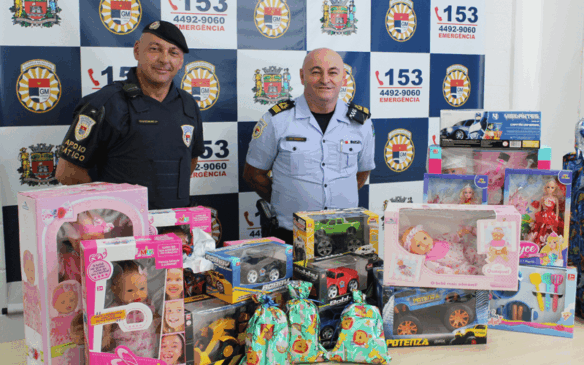 Membros da GMJ atrás de mesa com brinquedos arrecadados