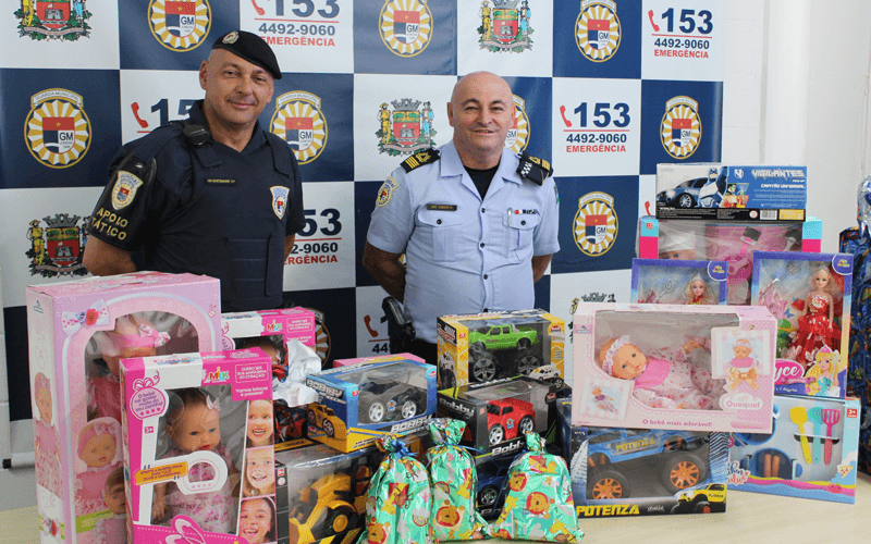 Membros da GMJ atrás de mesa com brinquedos arrecadados
