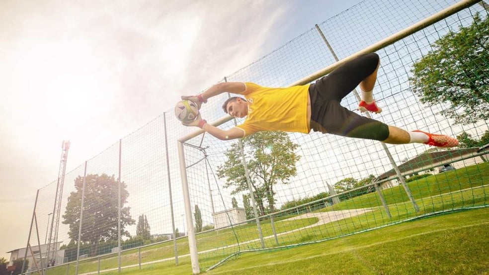 Goleiro de futebol em ação, defendendo uma bola durante um jogo.