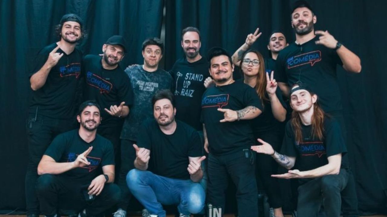 Grupo de comediantes posando para foto, sorrindo e fazendo gestos.