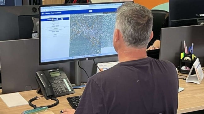Homem consulta cadastro fiscal imobiliário em computador, mostrando mapa da região de Jundiaí.