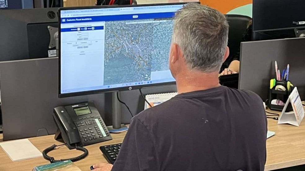 Homem consulta cadastro fiscal imobiliário em computador, mostrando mapa da região de Jundiaí.