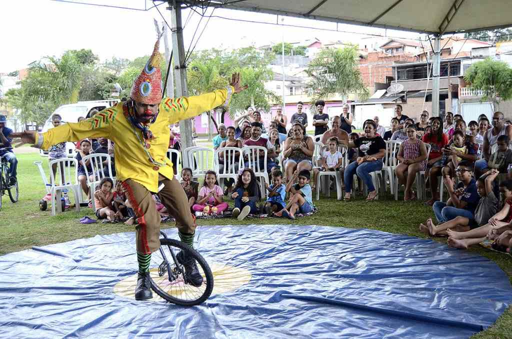 Homem em cima de um monociclo com crianças ao redor