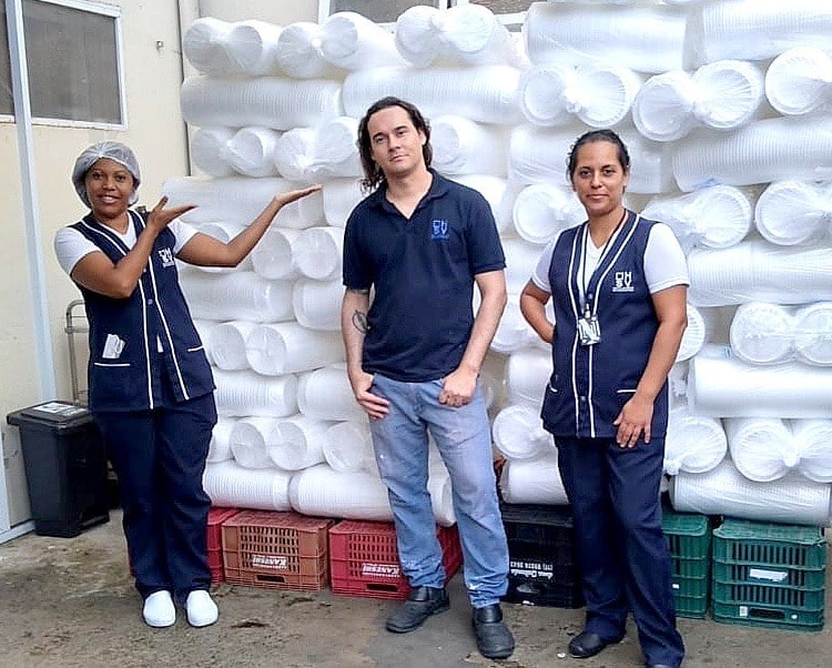 Foto de colaboradores na frente de pilhas de embalagens descartáveis
