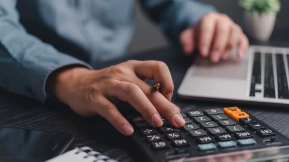 Homem mexendo em calculadora e computador.