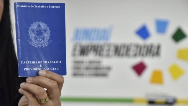Mulher segurando carteira de trabalho em frente a mural do Jundiaí Empreendedora - portal tem vagas de emprego abertas