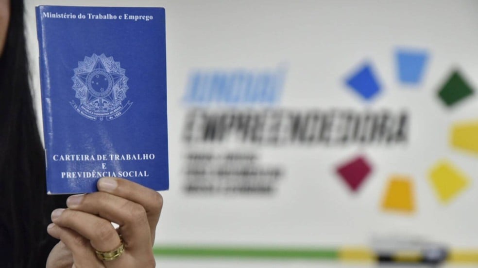 Mulher segurando carteira de trabalho em frente a mural do Jundiaí Empreendedora - portal tem vagas de emprego abertas