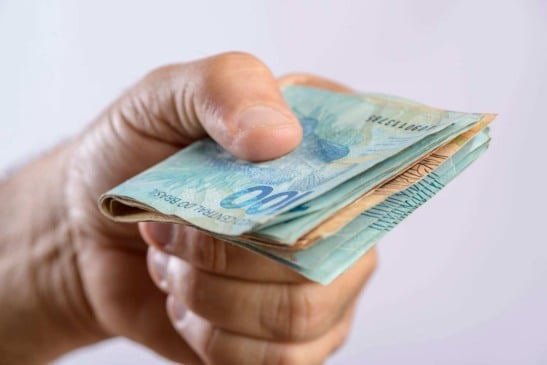 Mão segurando notas de real brasileiro, representando o aumento do salário mínimo previsto para 2025.