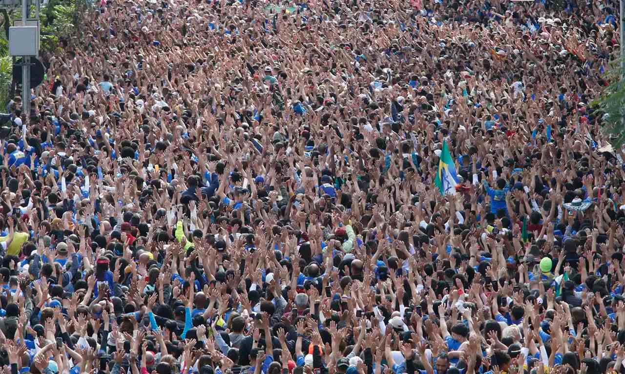 multidão participando da Marcha para Jesus 2024, com muitas pessoas de mãos levantadas, ao ar livre.