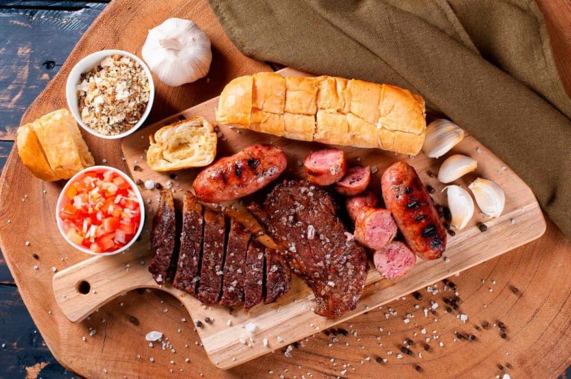 tábua com carnes de churrasco e acompanhamentos