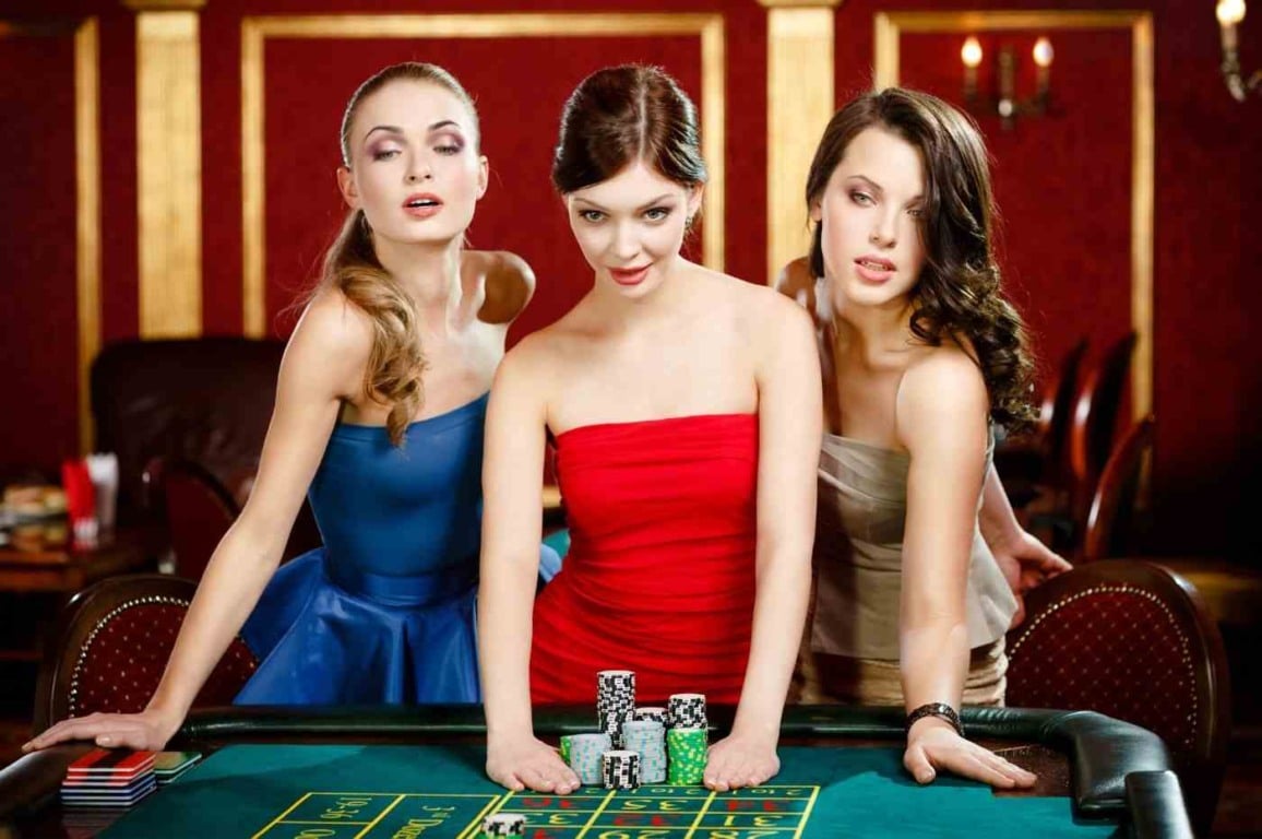 Três mulheres no mundo do iGaming em um cassino, elegantes ao redor de uma mesa de roleta com fichas de apostas. Três mulheres no mundo do iGaming em um cassino, elegantes ao redor de uma mesa de roleta com fichas de apostas.