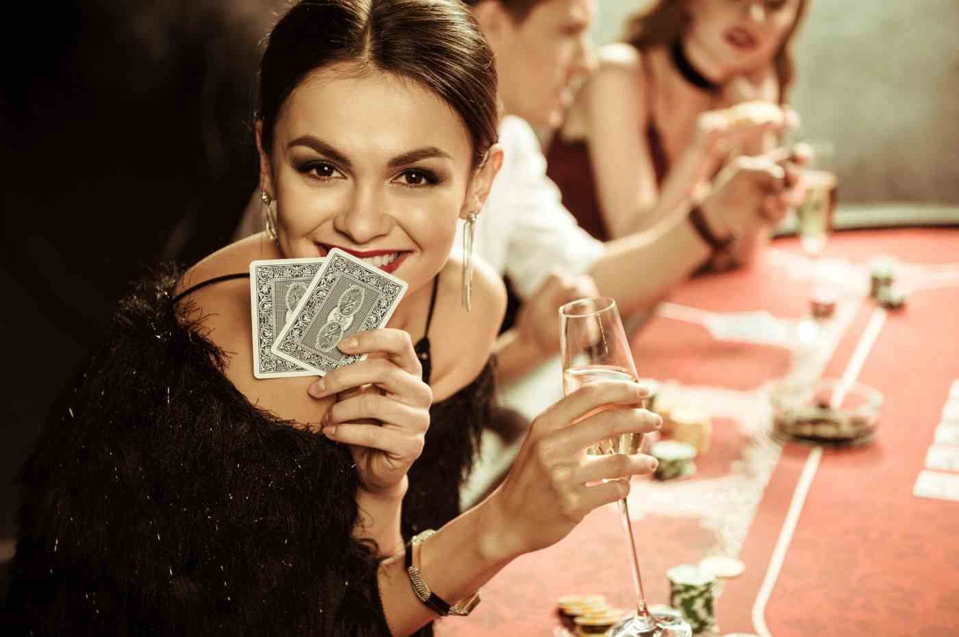 Mulheres no mundo do iGaming em mesa de pôquer, destaque para jogadora sorrindo com cartas na mão e taça de champanhe.