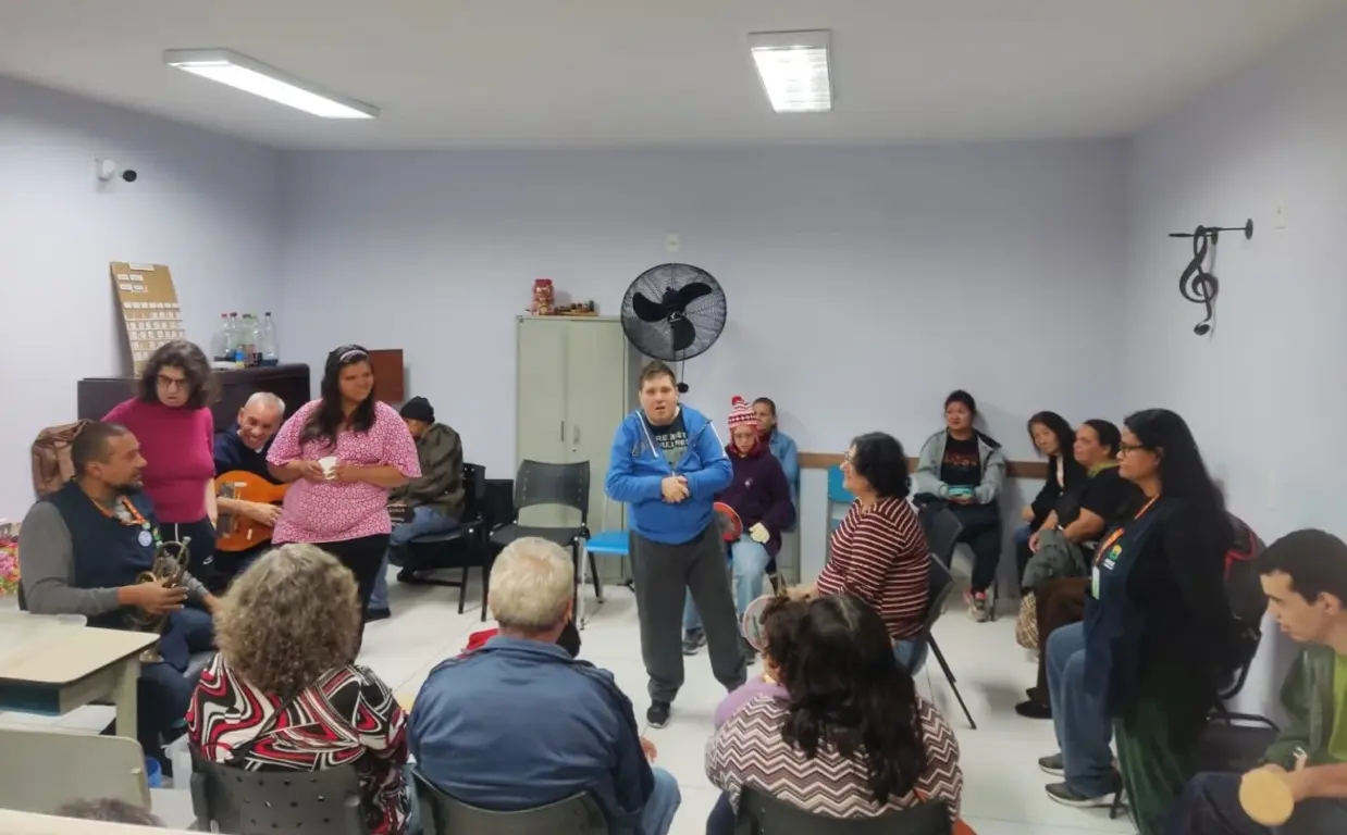 Atividade de musicoterapia na APAE Jundiaí com familiares e assistidos reunidos em roda, interagindo e participando de atividades musicais.
