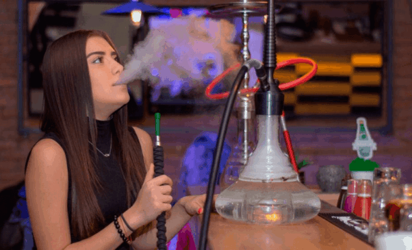 Garota jovem fuma narguilé em tabacaria