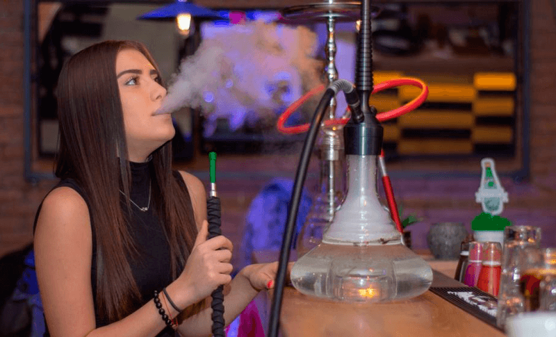 Garota jovem fuma narguilé em tabacaria