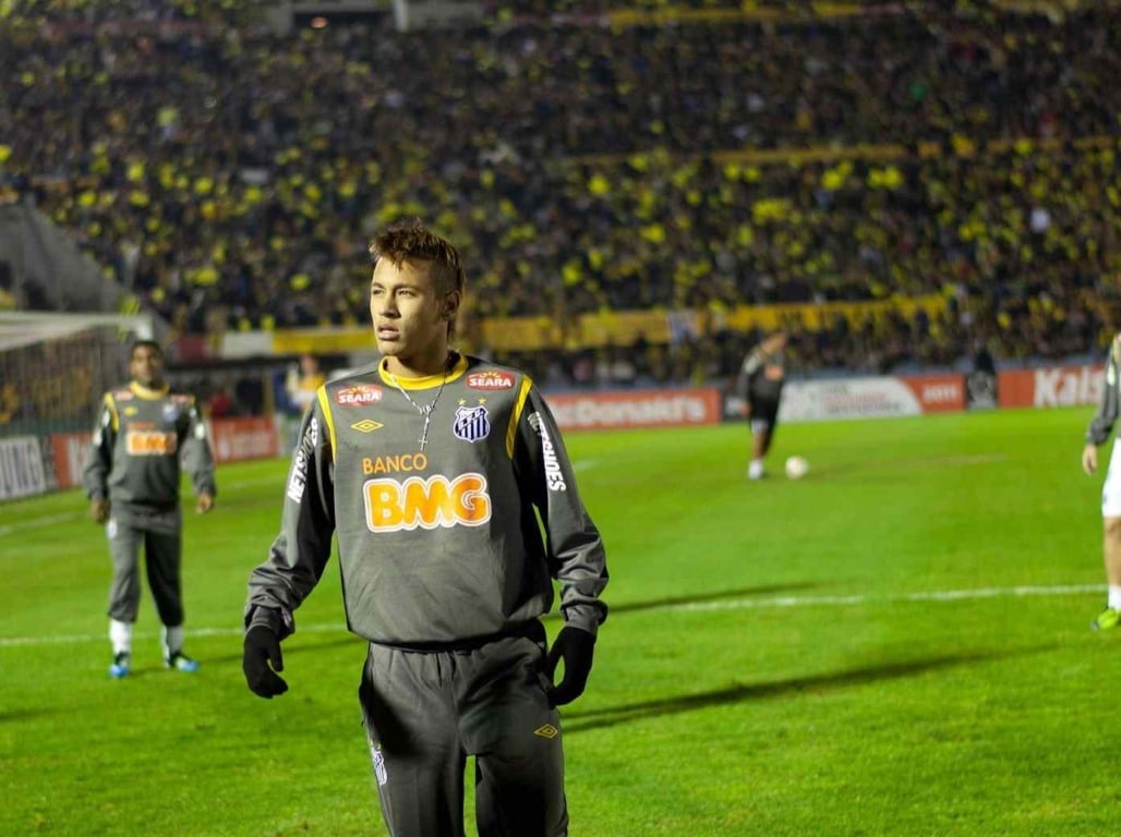 Neymar Jr com uniforme de frio do Santos FC em um campo de futebol a noite