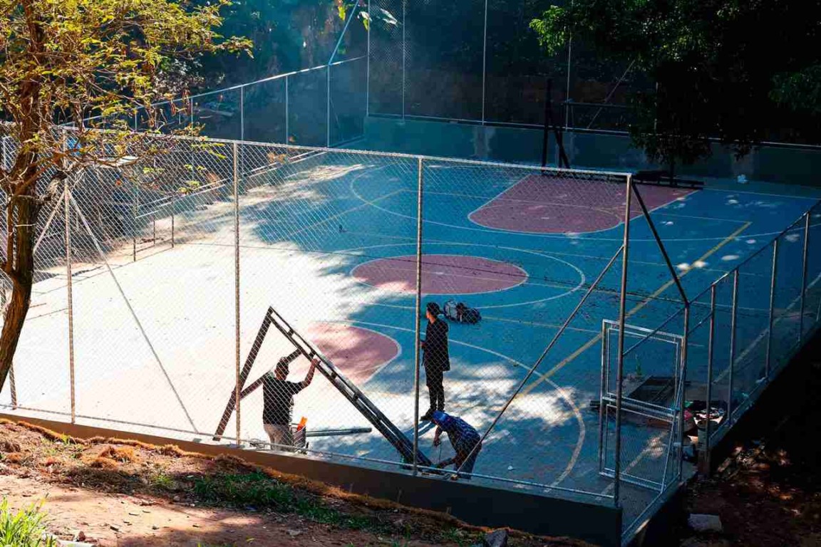 Construção de uma quadra poliesportiva como parte das novas opções de lazer em Jundiaí, com trabalhadores instalando alambrado.