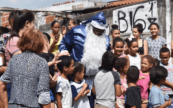 Papai Noel vestido de azul abraçando crianças
