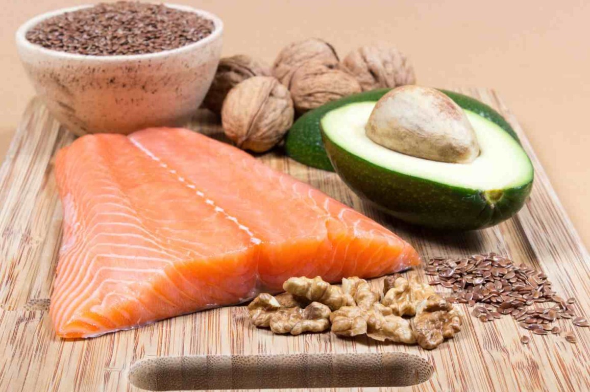 Filé de salmão, abacate, nozes, sementes de linhaça e uma tigela de sementes de linhaça em uma tábua de madeira, ricos em ácidos graxos ômega-3