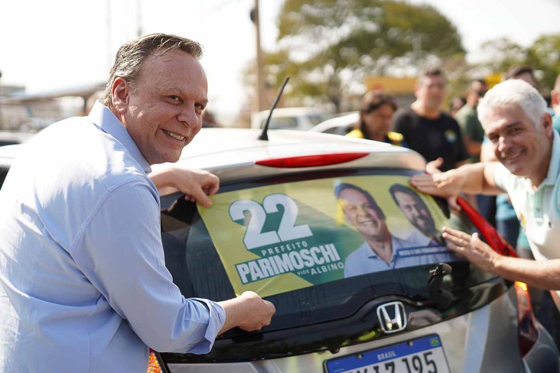 Parimoschi sorrindo enquanto cola adesivo de campanha em carro, marcando o início de sua corrida à Prefeitura de Jundiaí.