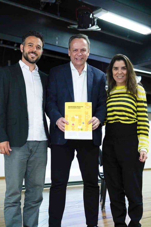 Parimoschi segurando documento ao lado de duas pessoas, simbolizando compromisso com políticas para a infância em Jundiaí.