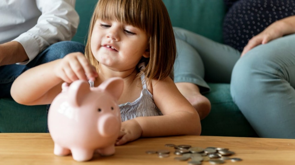 Menina guardando moedas em um cofrinho Menina guardando moedas em um cofrinho
