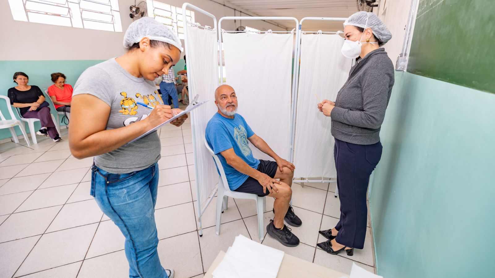 Idoso sentado em uma cadeira recebe atendimento de profissionais de saúde durante atividade do Mês da Pessoa Idosa na UBS Eloy Chaves, em Jundiaí.