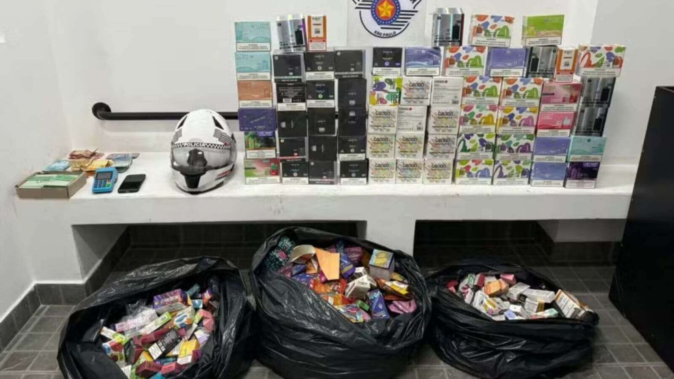 Caixas de cigarros eletrônicos em mesa e em sacos pretos com painel da Polícia de Jundiaí Caixas de cigarros eletrônicos em mesa e em sacos pretos com painel da Polícia de Jundiaí