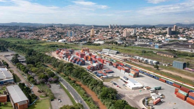 Terminal Intermodal de Jundiaí visto de cima, com contêineres coloridos organizados em pátio logístico, linhas férreas e parte da cidade ao fundo.