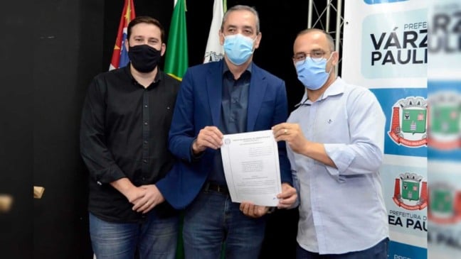 três homens segurando um papel na frente de um painel