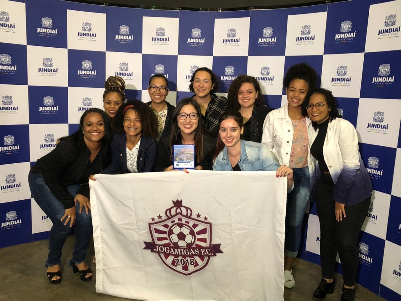 Foto de time de futebol feminino segurando bandeira 