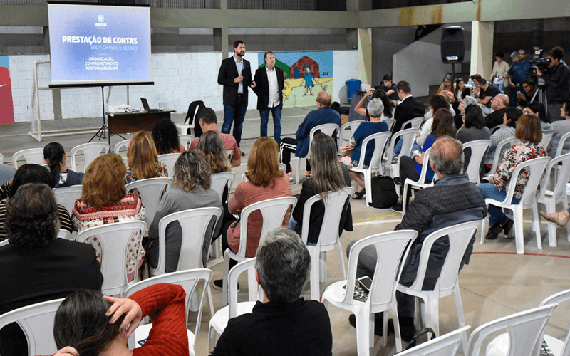 Foto ampla dos participantes sentados em frente ao prefeito Luiz Fernando Machado e vereador Albino