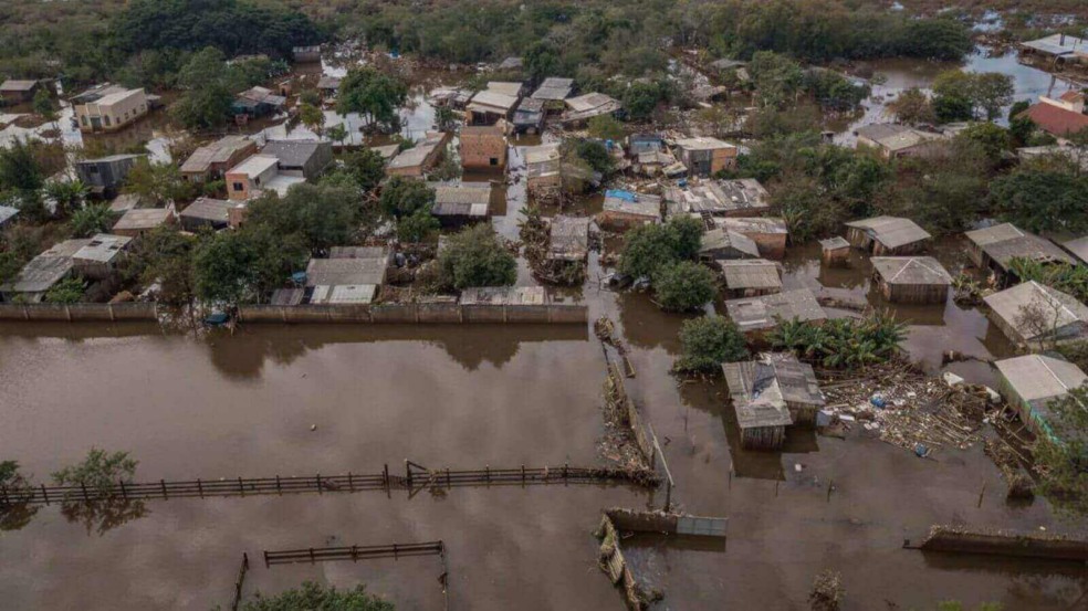 Bairro alagado após enchente, mostrando casas inundadas e danos causados pela água em uma comunidade do Rio Grande do Sul.