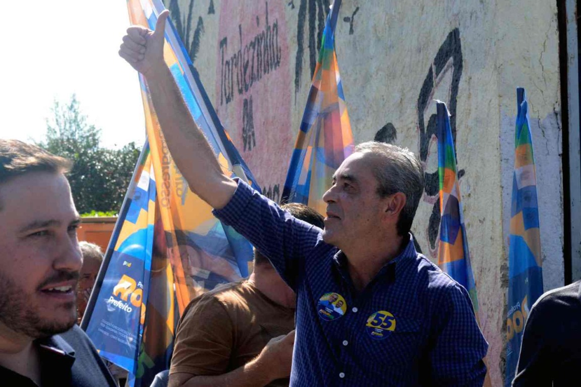 Prefeito Rodolfo Braga acena para apoiadores em caminhada no Jardim Promeca, cercado por bandeiras e equipe de campanha.