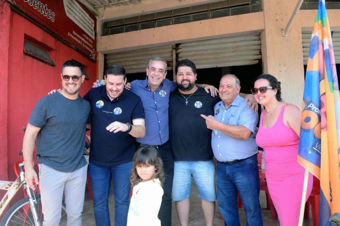 Prefeito Rodolfo Braga posa sorridente com apoiadores e moradores em frente a comércio no Jardim Promeca durante campanha.